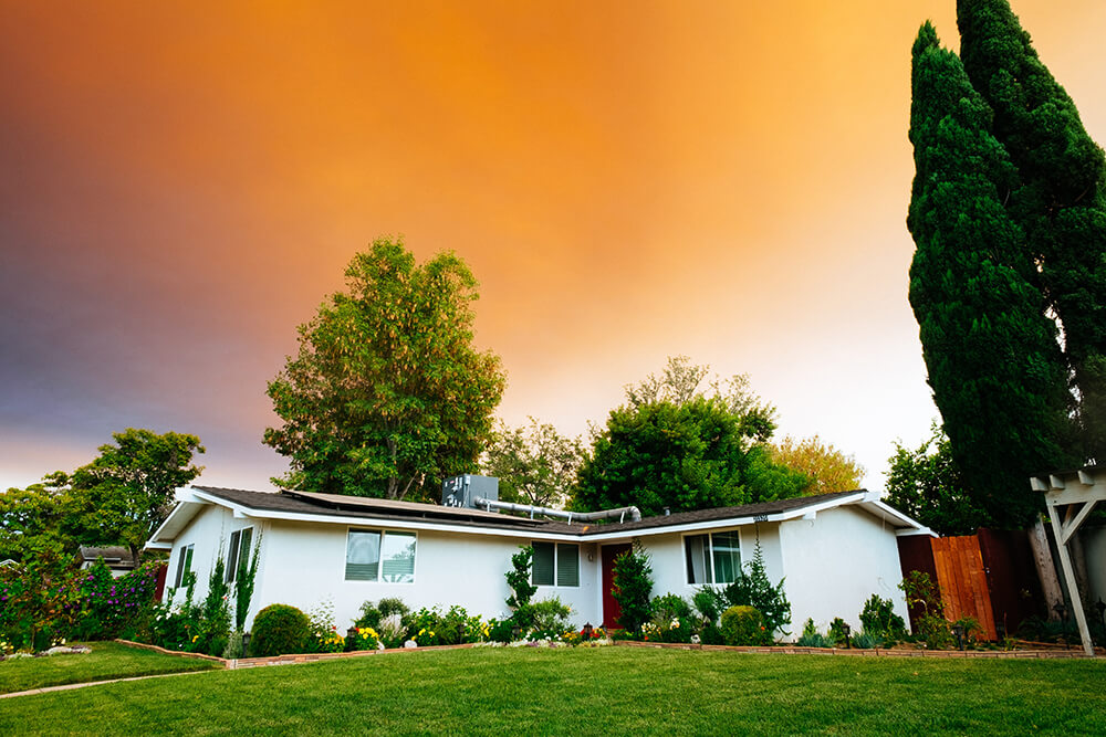 A beautiful one story house surrounded by greenery with orange sky above it